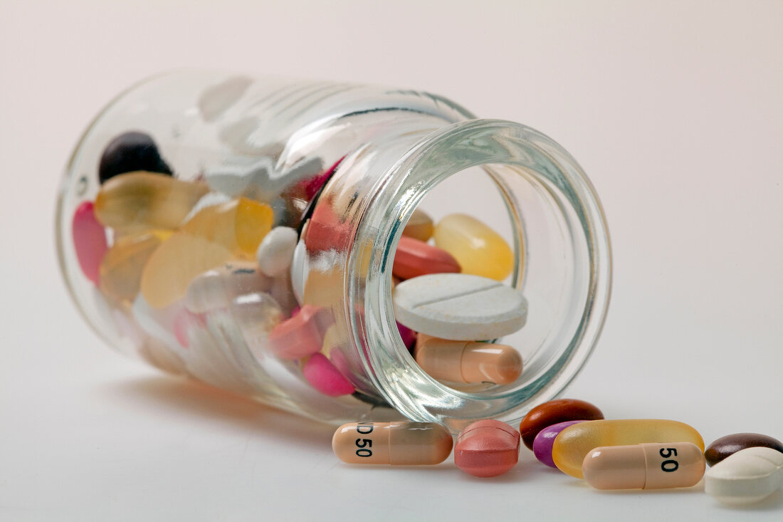 Different pills, tablets, dragees and capsules spilling out from glass bottle