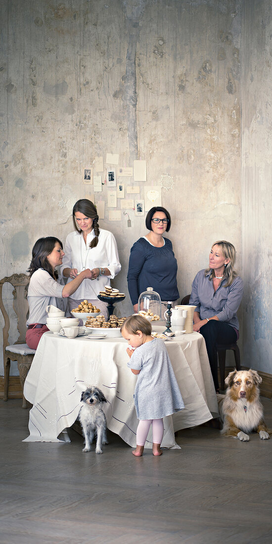 Women sitting and standing around table and child standing besides with dogs