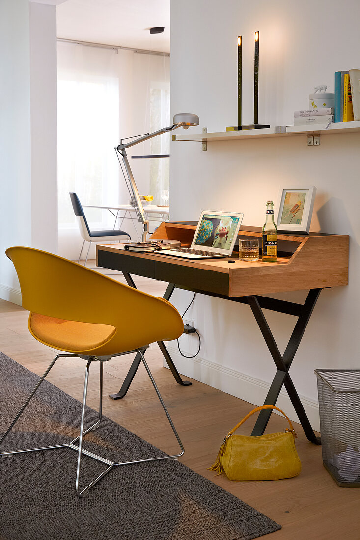 Laptop on secretary desk with yellow chair and table lamp in working area