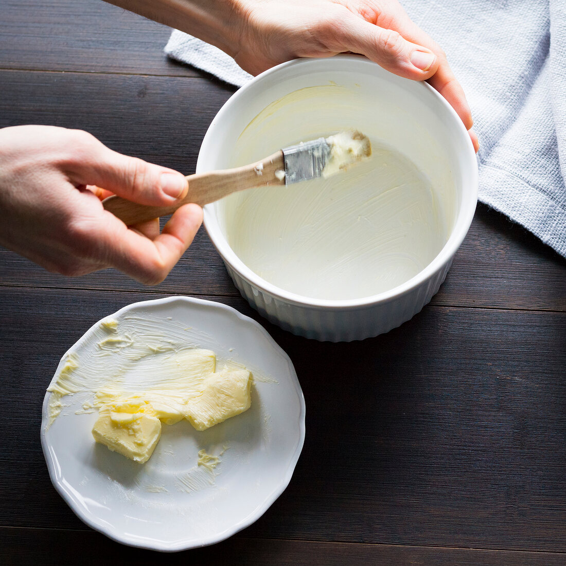 Close-up of man's hand greasing with butter in baking bowl on wooden table