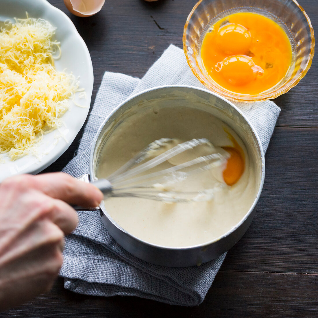Close-up of man's hand whisking grated cheese and eggs in sauce pan