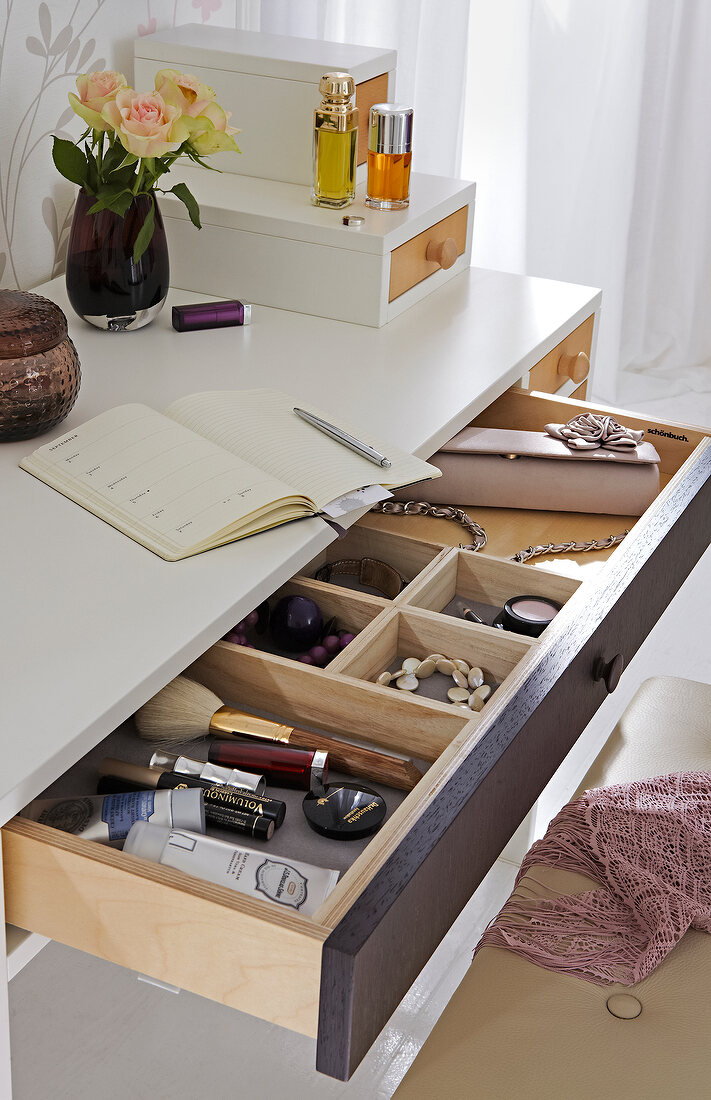Diary, vase and perfume on dressing table while accessories and cosmetics in open drawer