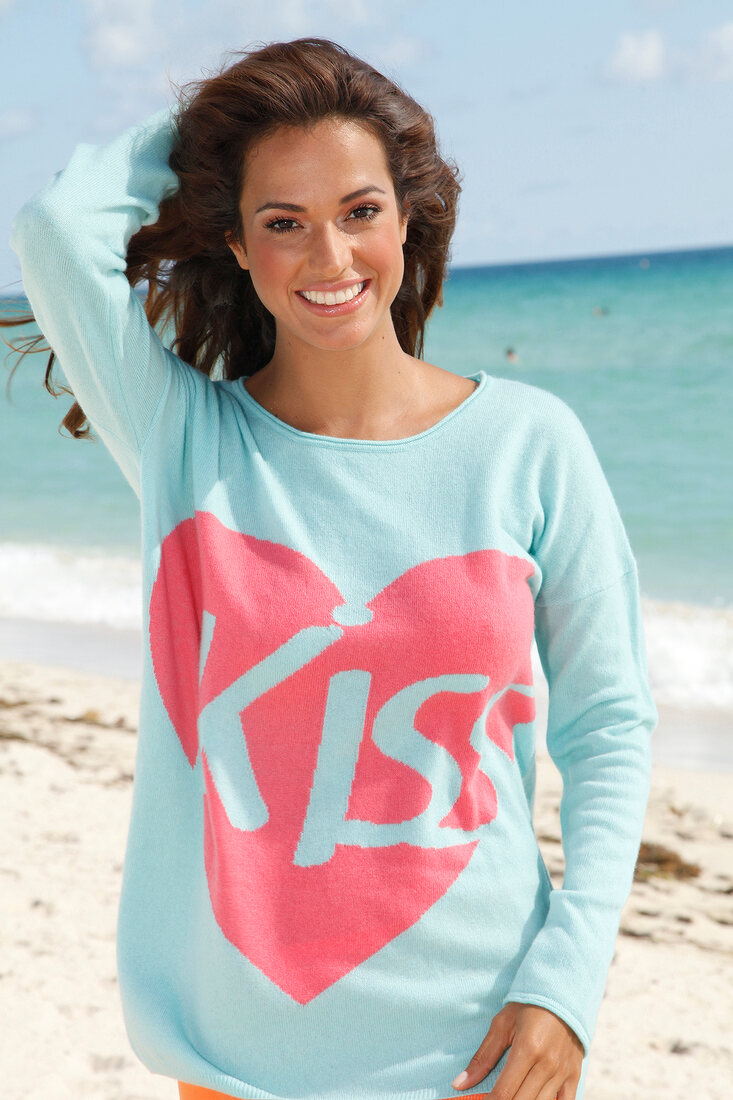 Portrait of pretty woman with dark windswept hair wearing blue top standing on beach