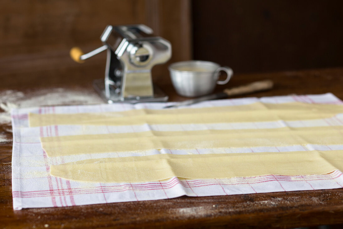 Woman making homemade noodles with pasta machine on table