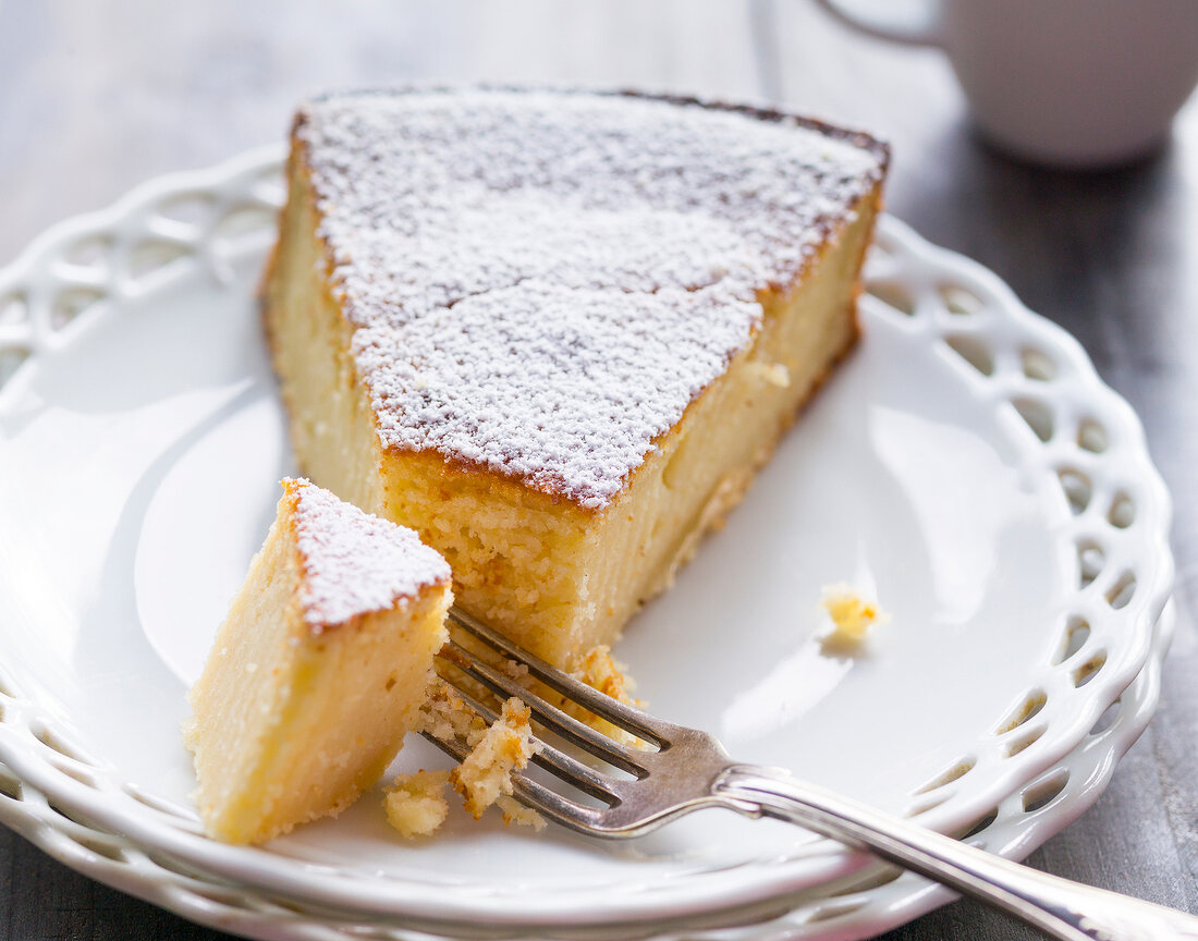 Slice of lemon almond cake with icing sugar and fork on plate