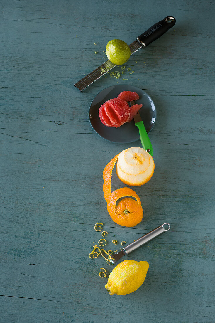 Various citrus fruits, peeler and knives on green background, overhead view