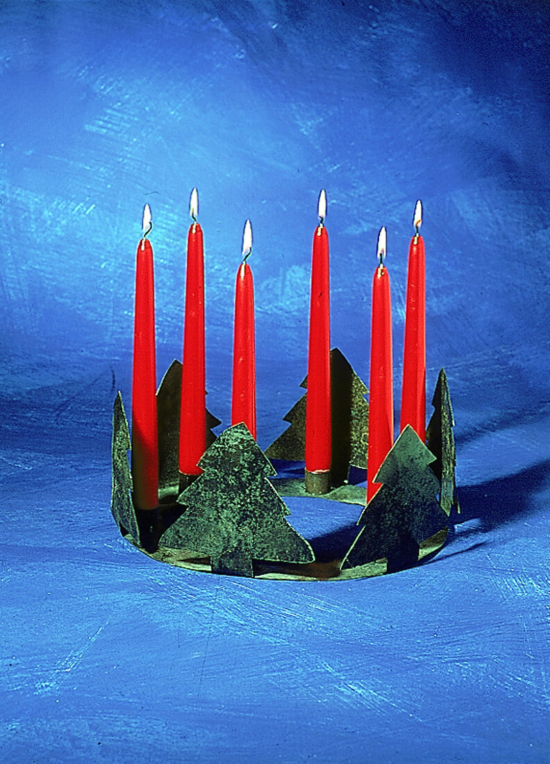 Kranz aus grünem Metall mit roten Stabkerzen vor blauem Hintergrund