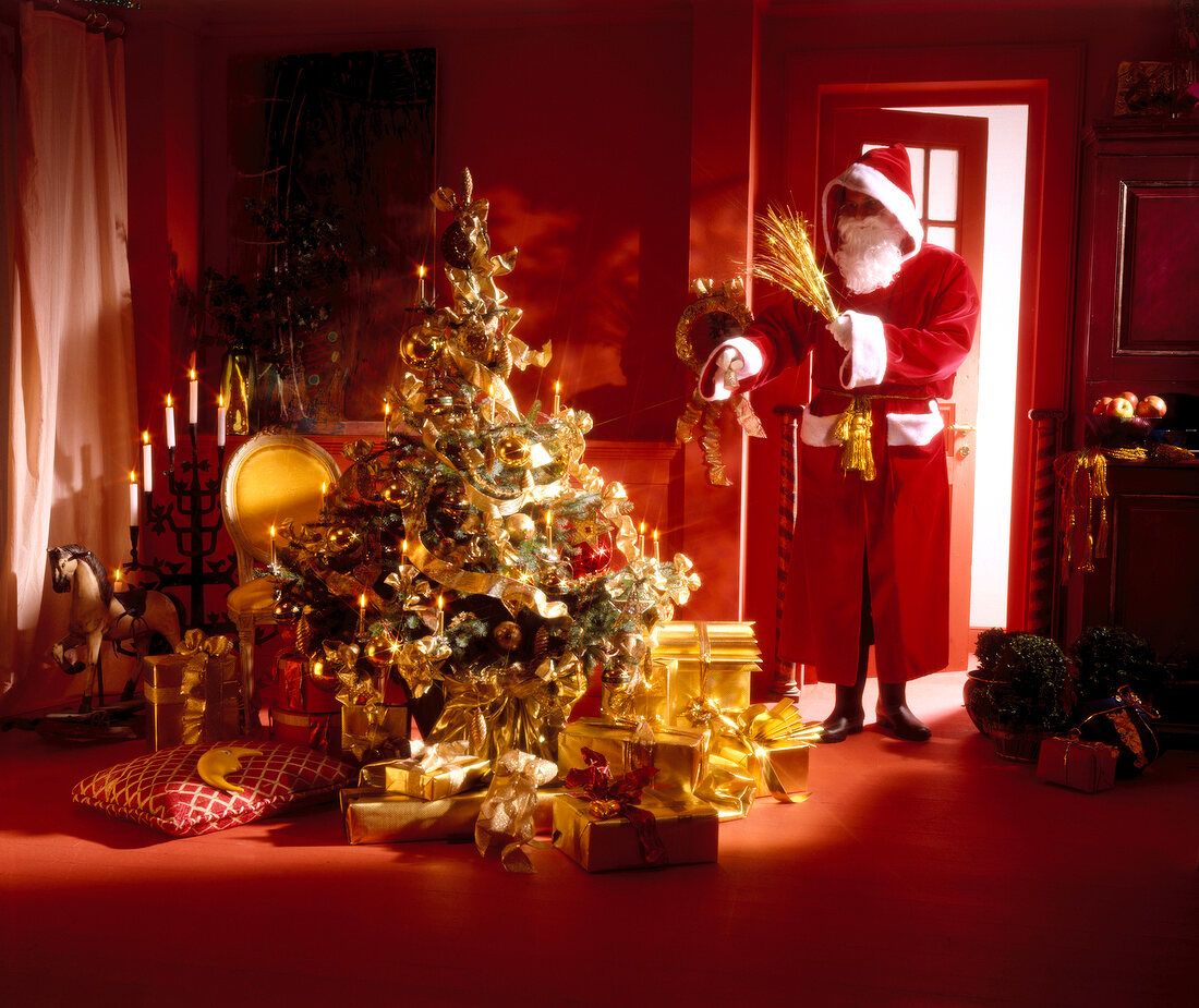 Santa Claus standing with goldenrod near decorated Christmas tree