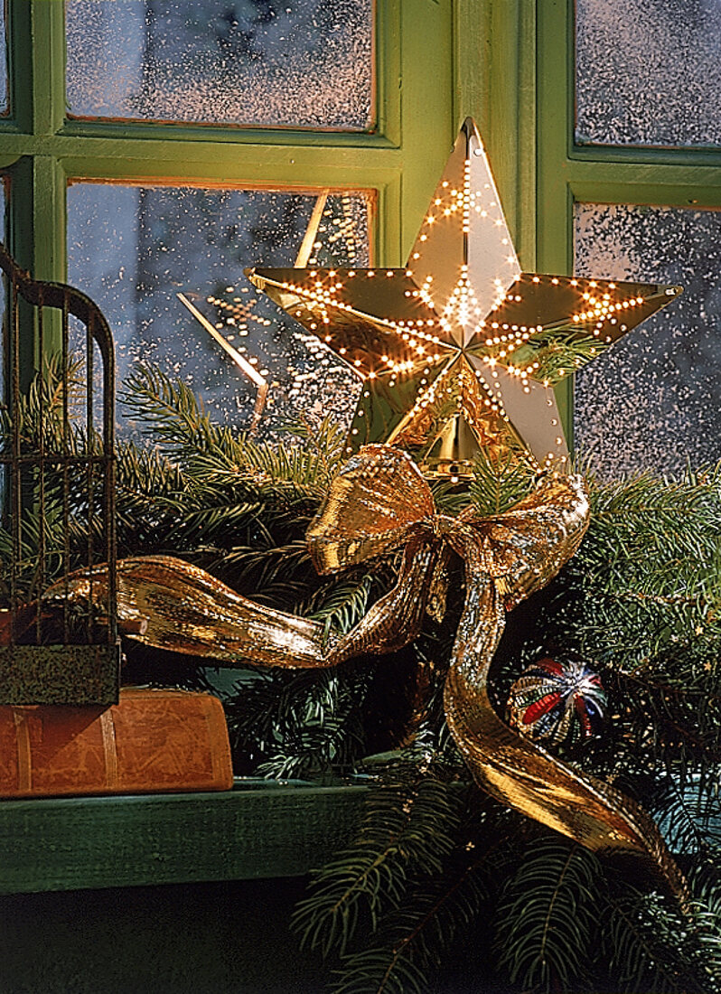 Adventsgesteck mit Goldstern auf Fensterbank, beleuchtet