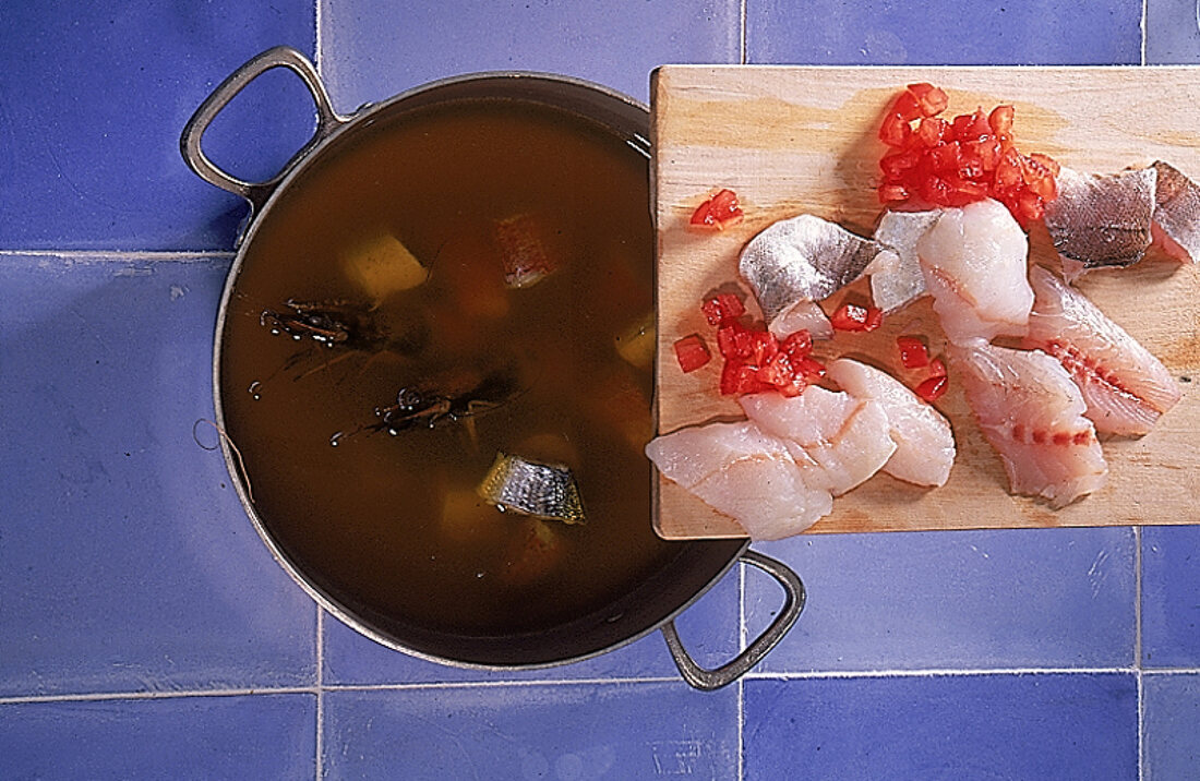 Topf von oben auf blauen Kacheln, darüber ein Brett mit  Fischstücken