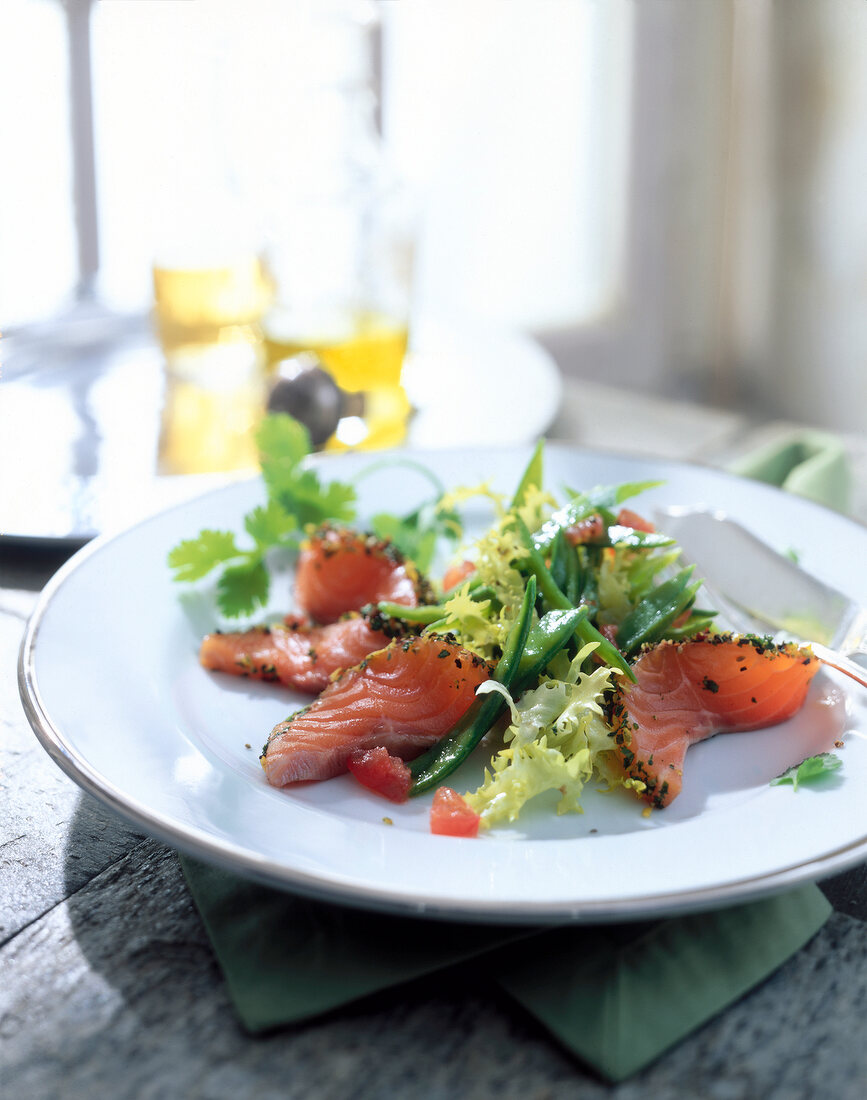 Close-up of marinated salmon with sugar snap peas salad on a white plate