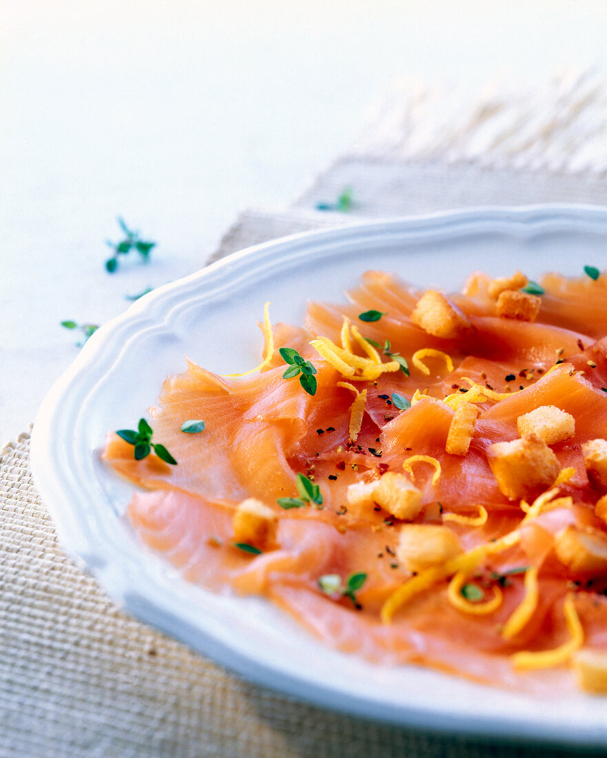 Close-up of salmon carpaccio with thyme walnut croutons and lemon strips served on plate