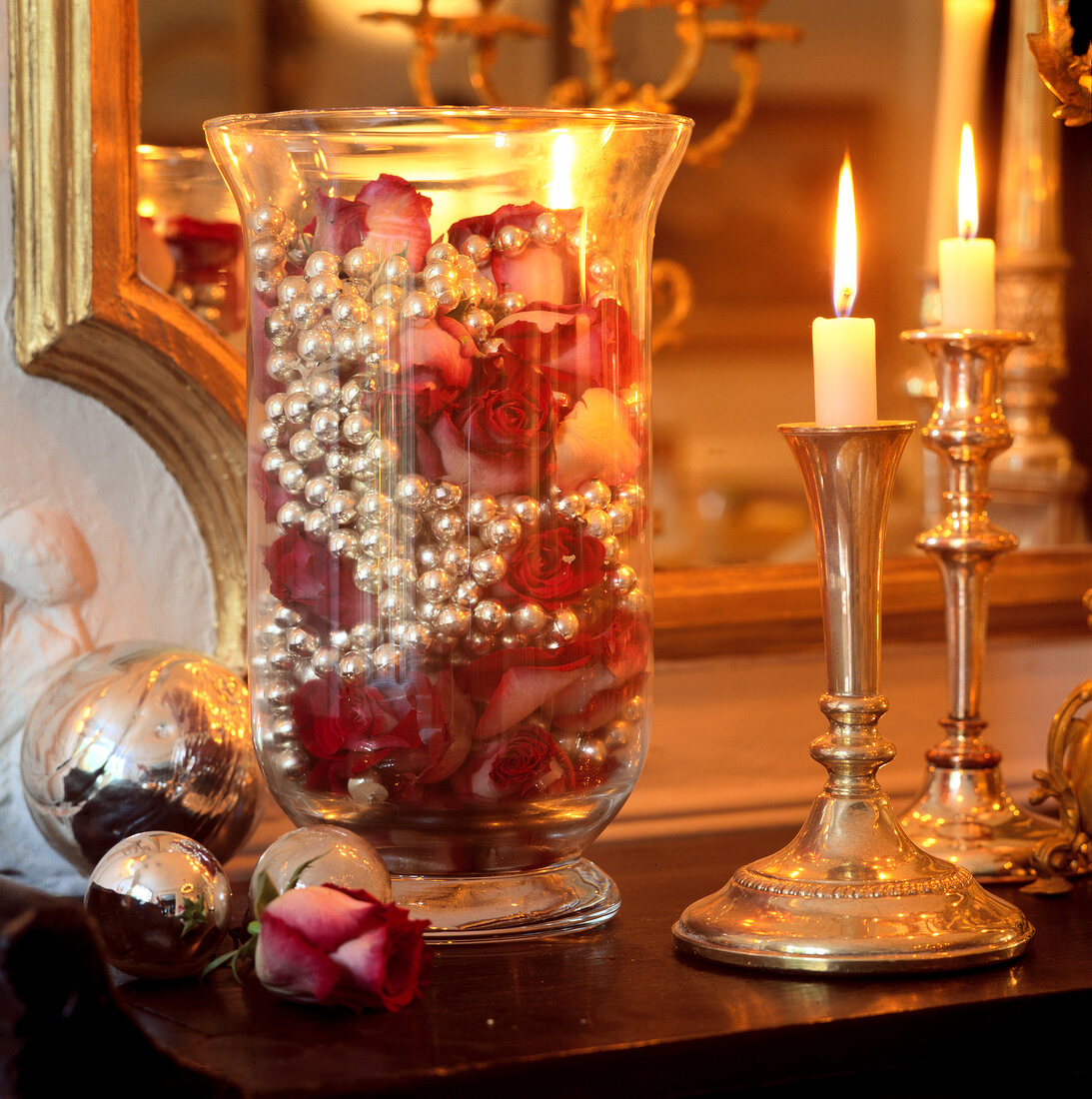 Roses and silver chain in large glass lantern beside lit candle