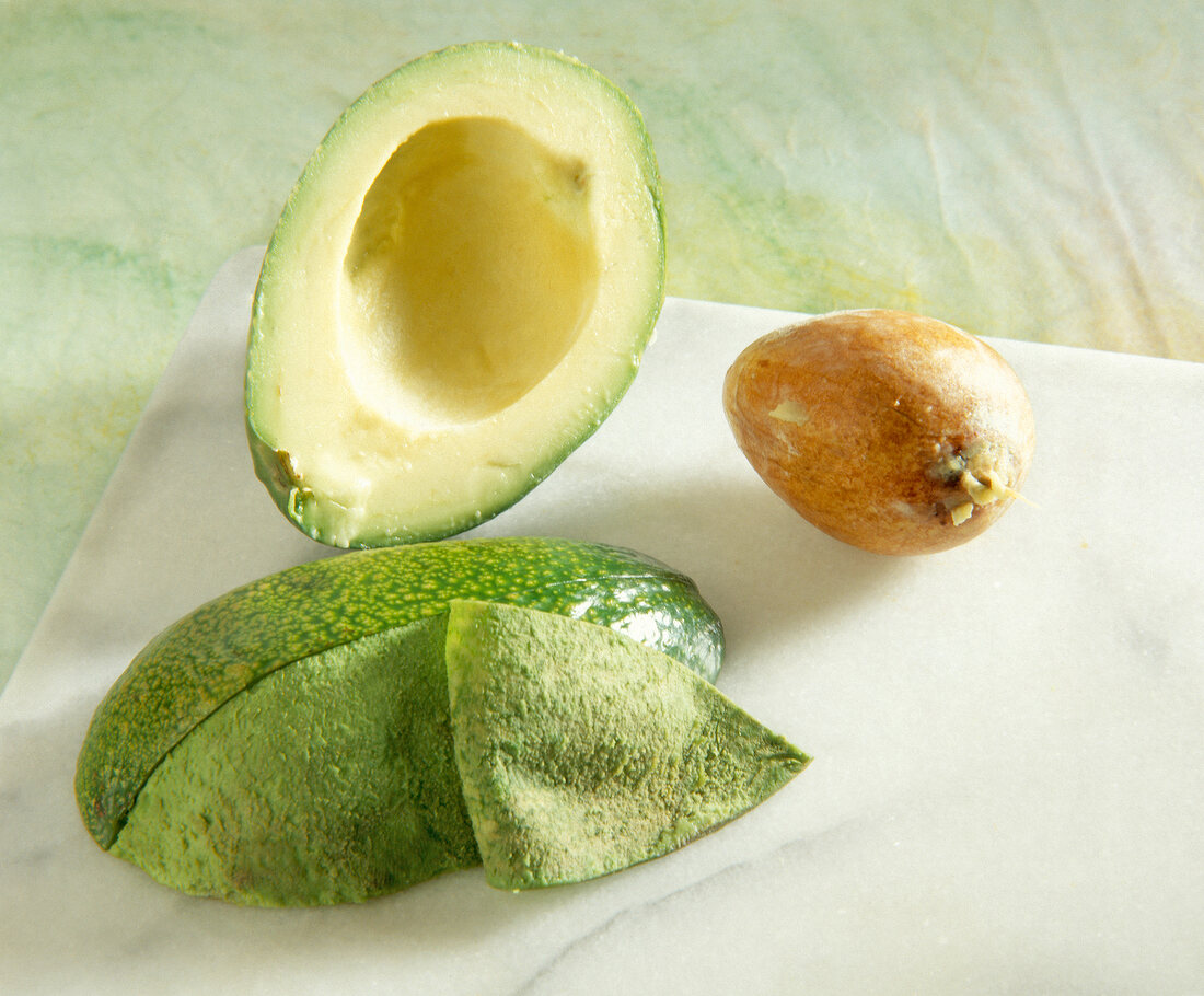 Halved avocado partially peeled with a stone on table