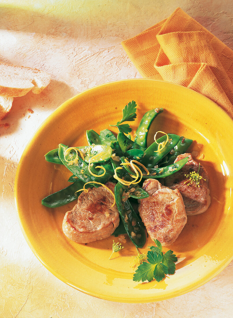 Schweinefilet mit Erbsen auf orangem Teller.