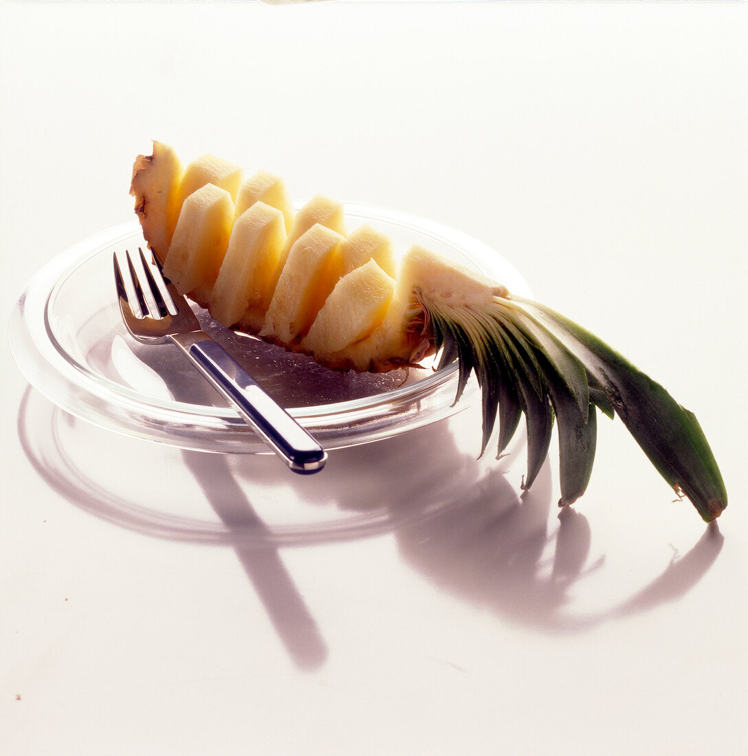 Cut slice of pineapple on glass plate with fork