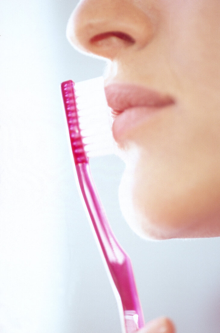 Side view of woman massaging her lips with pink toothbrush, close-up