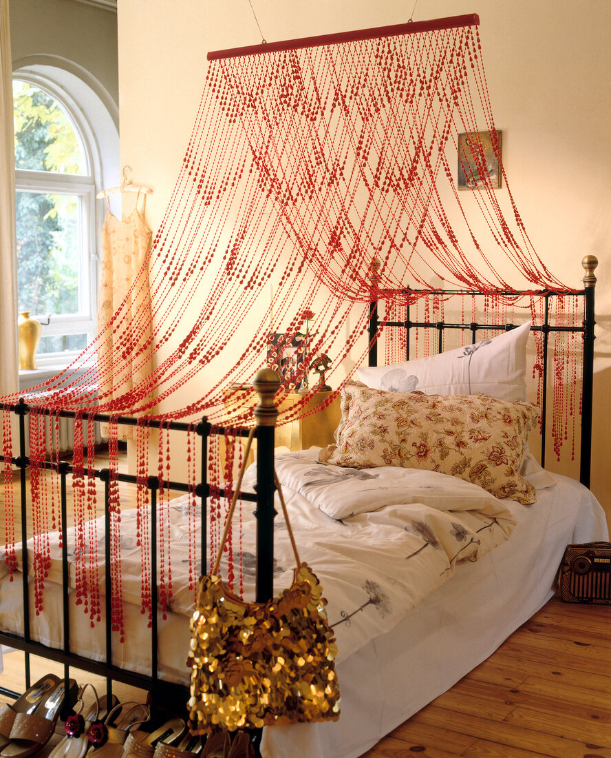 Red beaded curtains hang over the metal bed, floral pattern cushion