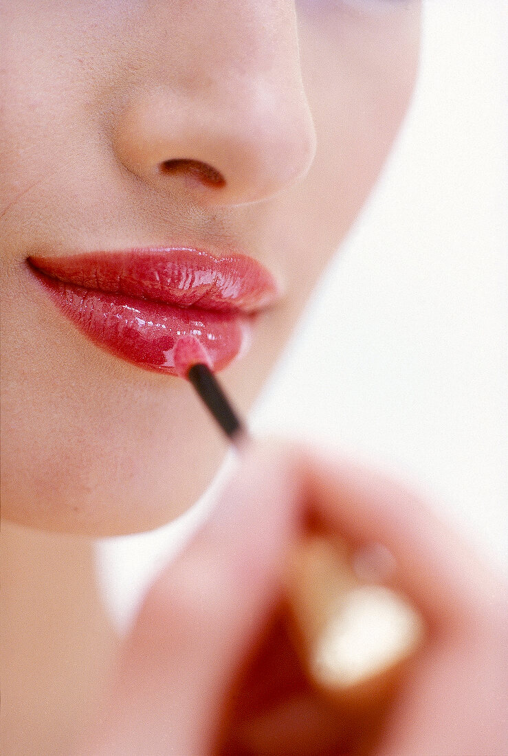 Close-up of woman applying red lip gloss with intense shine on