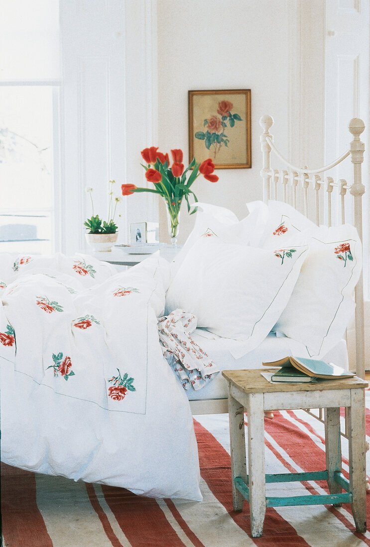 Room with white blanket and pillow with floral pattern design on bed