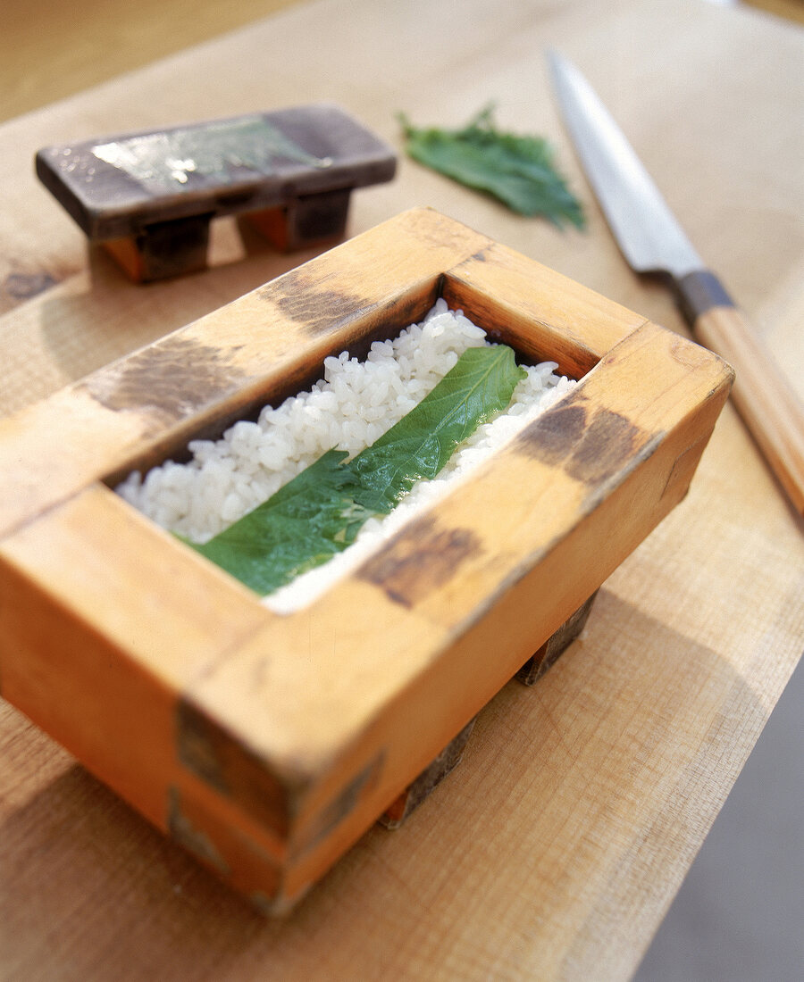 Step: Auf den Reis im Holzkasten werden dünne Streifen Shiso gelegt