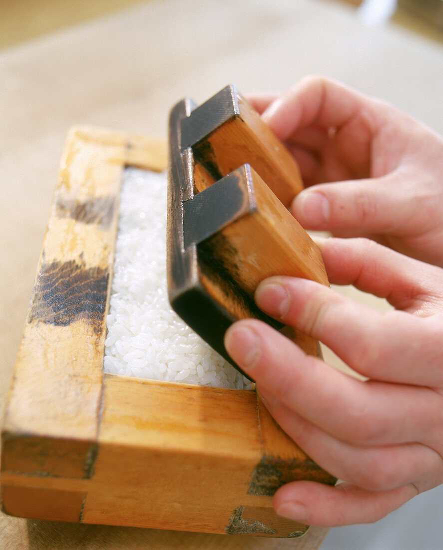 Step: Der Reis im Holzkasten wird mit Hilfe des Deckels festgedrückt