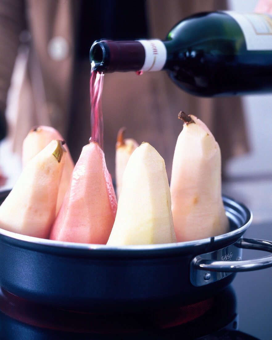 Red wine being poured on peeled pears for preparing dessert