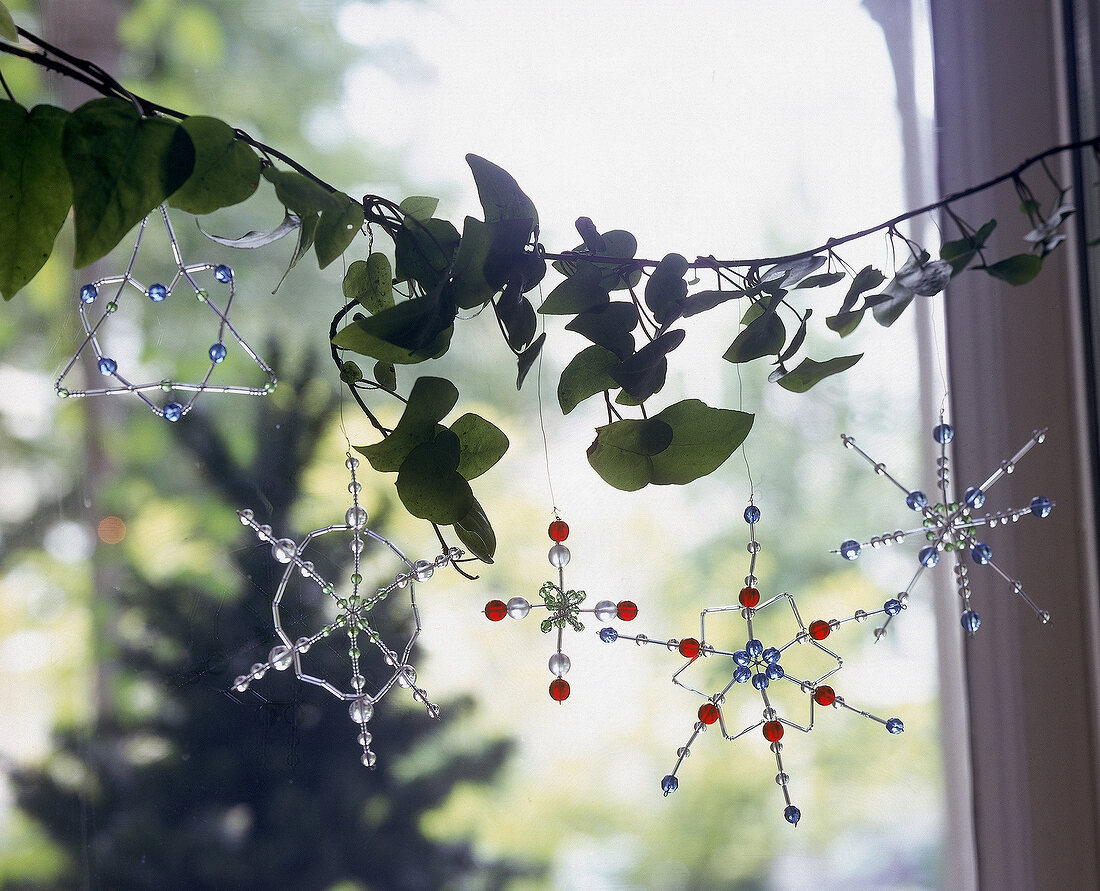 Schneeflocken aus Glasperlen und Silberdraht hängen an einer Pflanze