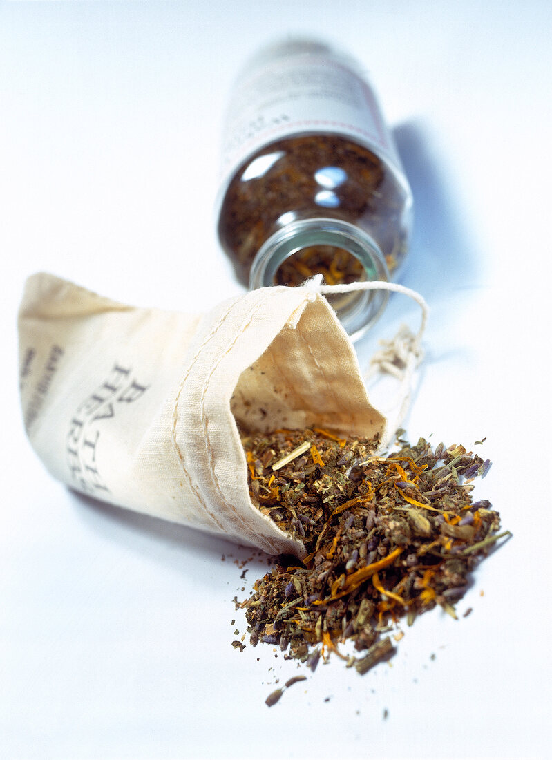 Herbal sachet and glass bottle filled with herbs on white surface