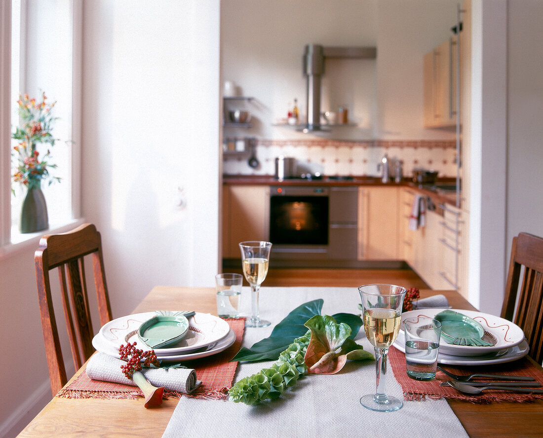 Table for two laid with wine glass and green fish bowl on plates, kitchen in background