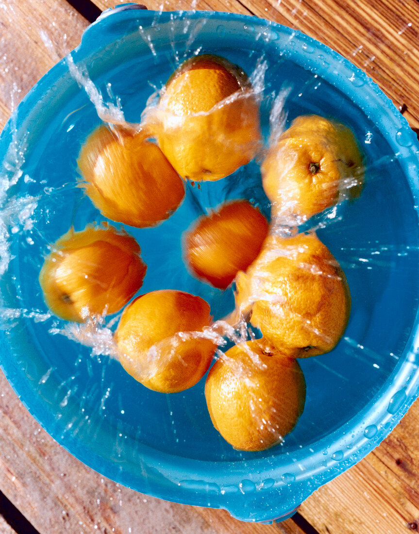 Orangen fallen von oben in einen vollen Eimer mit Wasser, Aufsicht