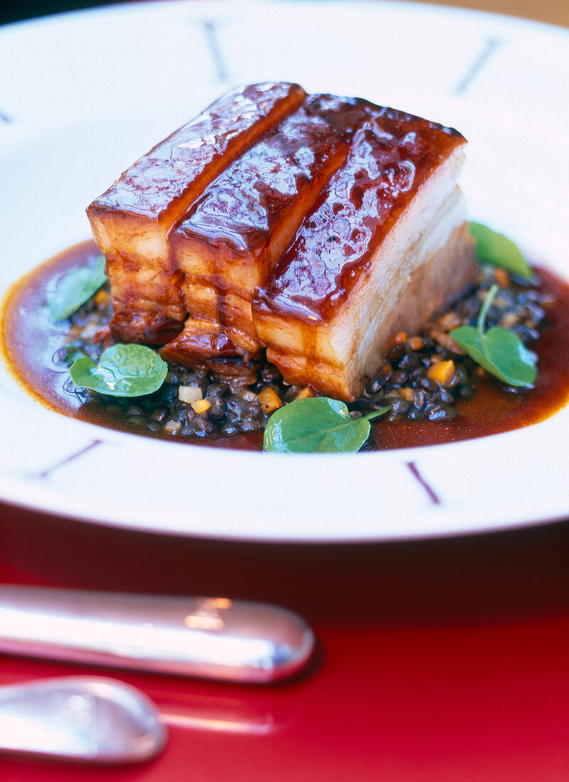 Close-up of fresh spiced pork belly with lentils in white plate