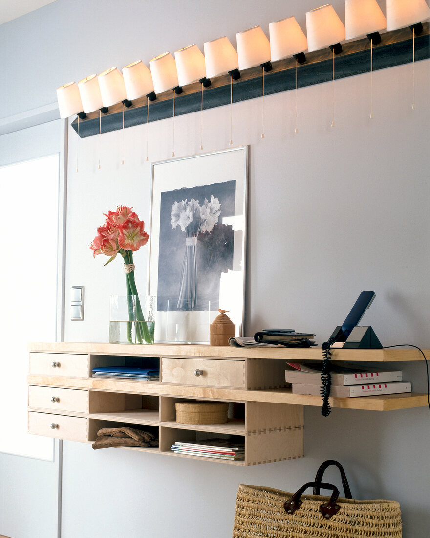 Wooden platform with small drawers under wall light with twelve lampshades