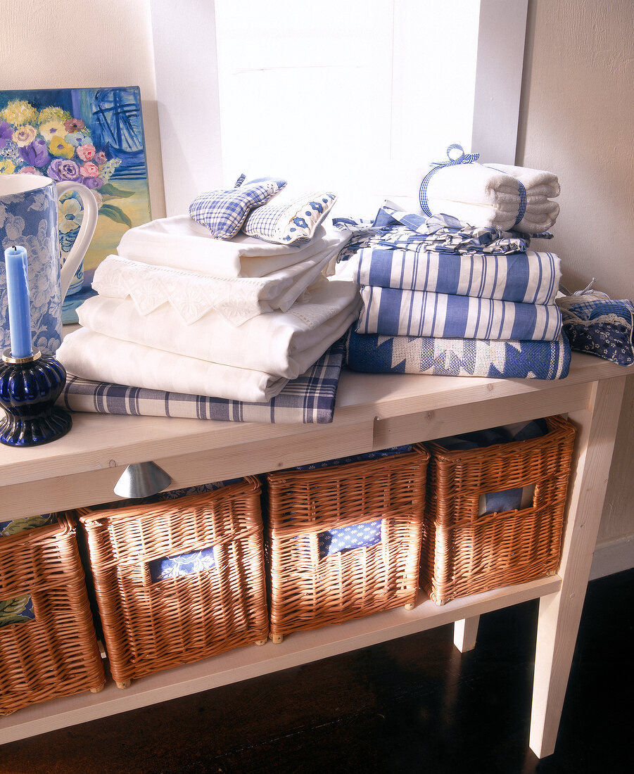 Stack of white towels and linen bed sheet with wicker drawers on pine wood sideboard