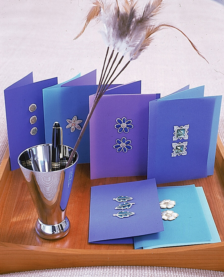 Blaue Briefkarten mit Stickmotive aufgestellt,silb. Gefäß m Kulli.