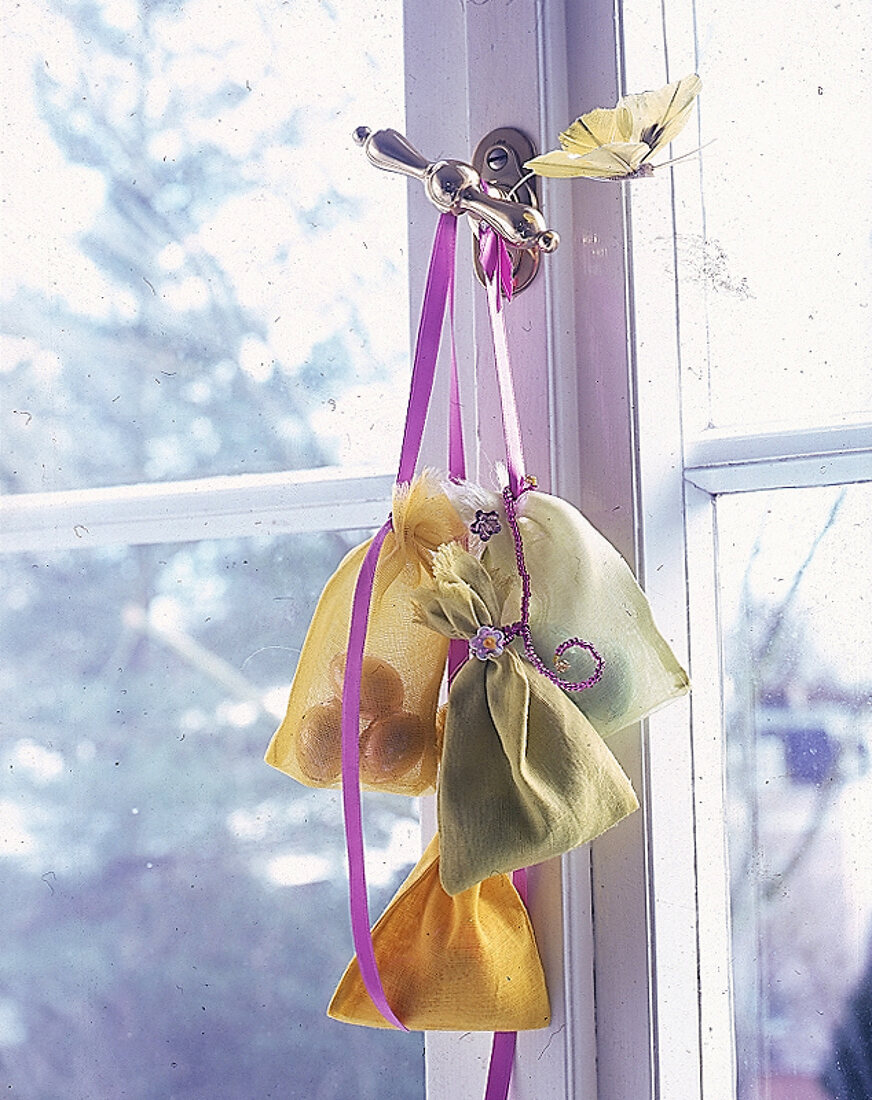 Stoffsäckchen mit Glasblüten und Perlenschnüre hängen am Fenster