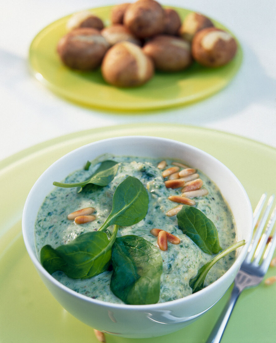 Bowl of spinach dip with sour cream and small potatoes on plate