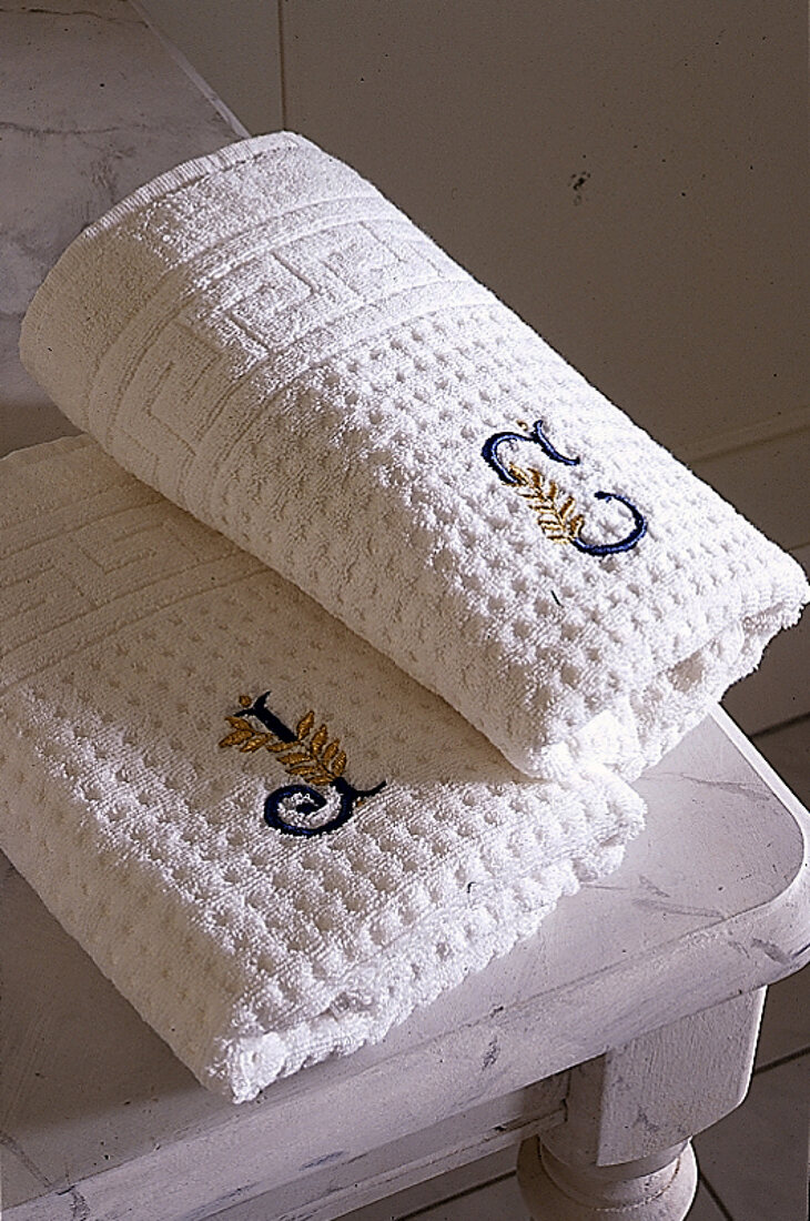 Zwei weiße Handtücher zusammengelegt liegen auf weißem Holzhocker.X