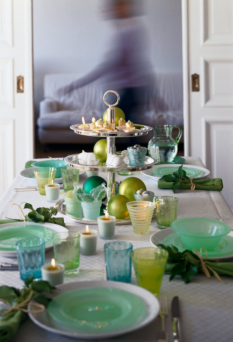 Tiered stand with candles, green plates, lit candles and glass on table