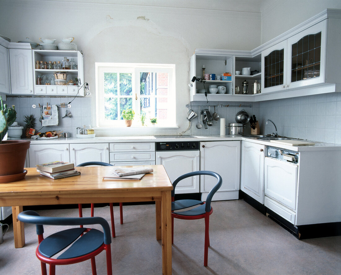 Interior of white kitchen with maple cabinets, blue-red two chairs and table