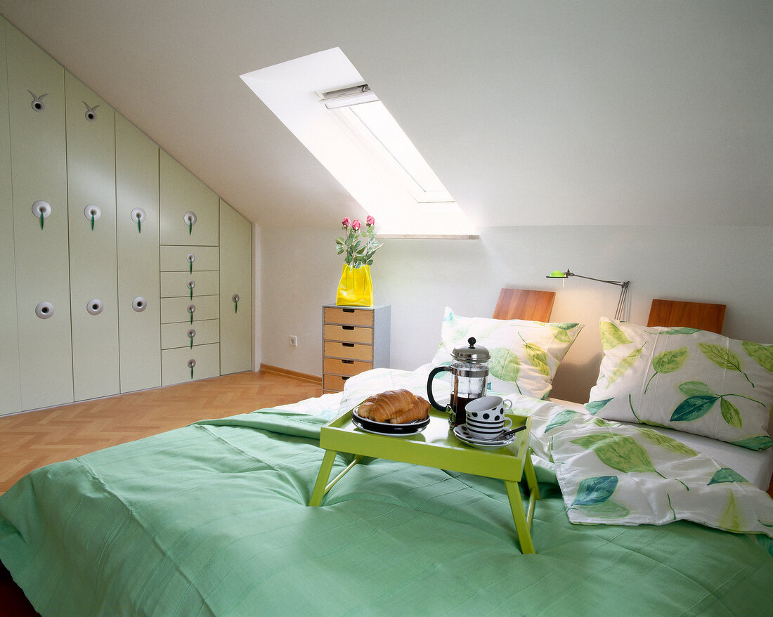 Bed with green bed sheet and small table in attic