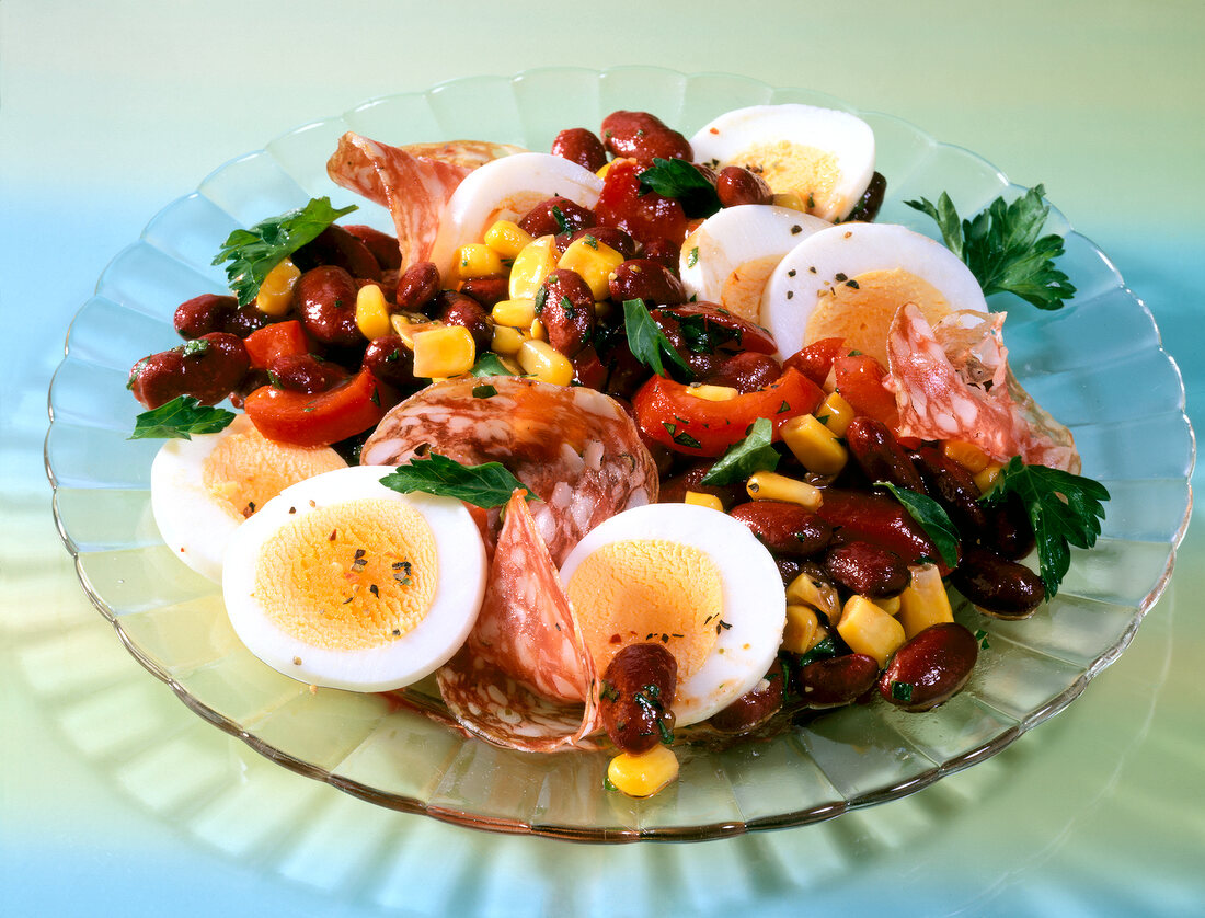 Egg salad with beans, corn and salami on glass plate