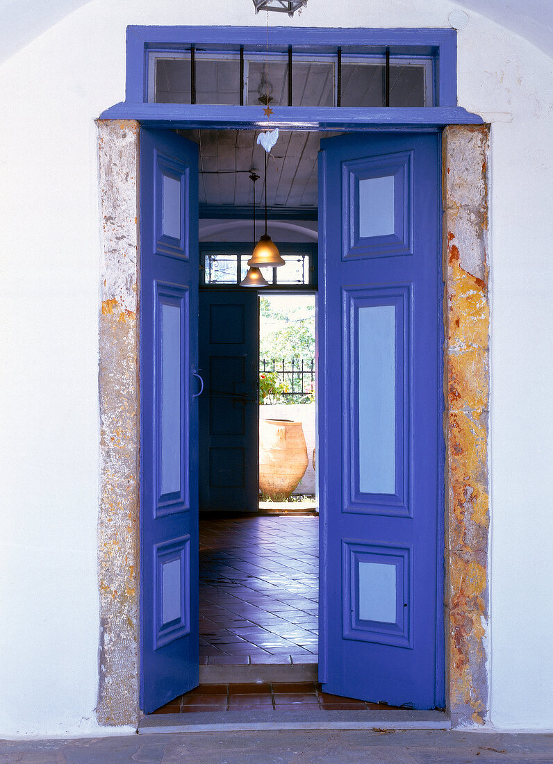 View of tiled hall and old water barrel through open wooden door