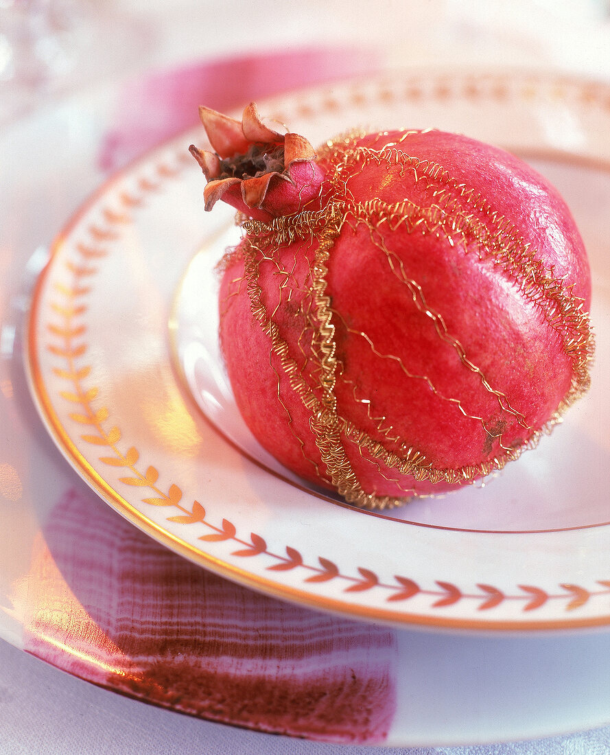 Tischdeko: Granatapfel mit Golddraht auf edlem Teller