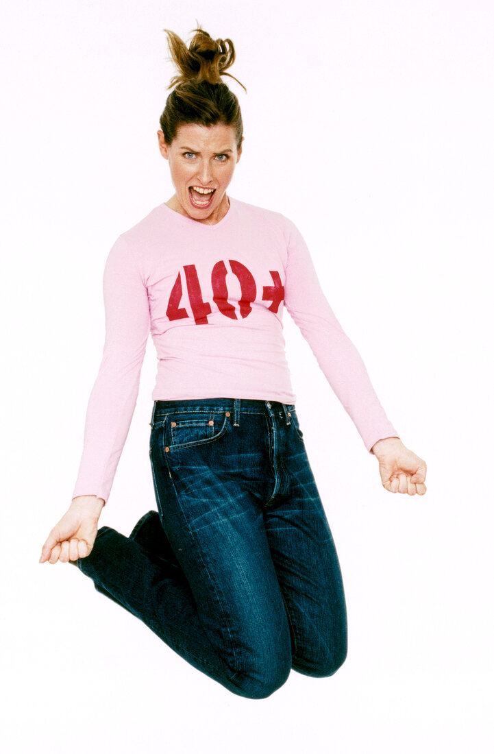 Excited woman in pink t-shirt with '40+' print jumping in air and screaming