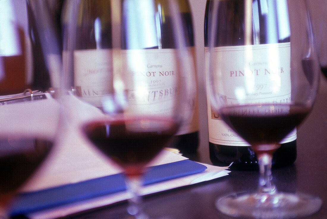 Flaschen mit Pinot Noir im Hintergrund, vorne gefüllte Rotweingläser