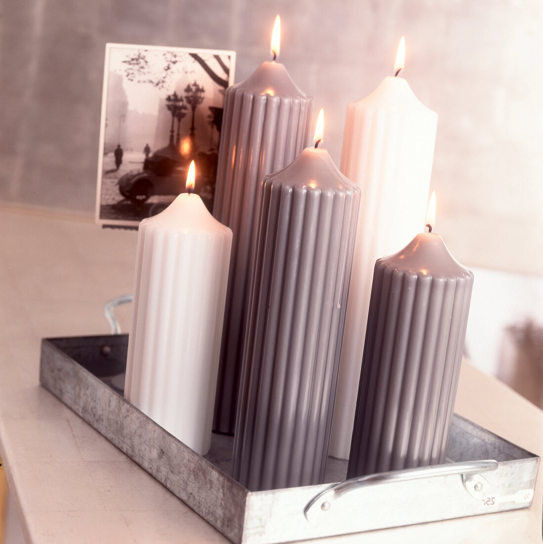 Variety of white and gray lit candles in metal tray