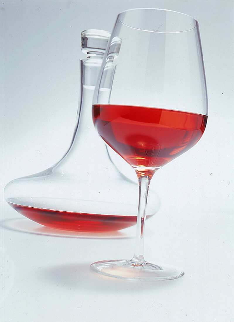 Glas Rotwein,dahinter eine Glaskaraf fe mit Wein