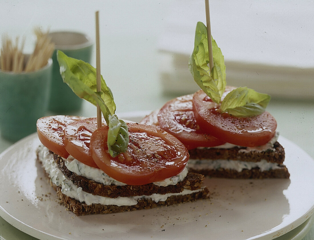 2 belegte Vollkornbrote mit Tomate und Quark, Basilikumscheibe