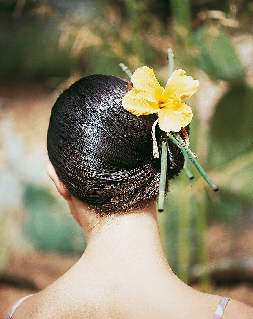 Frau hat ihr brünettes Haar mit einer gelben Blume festgesteckt